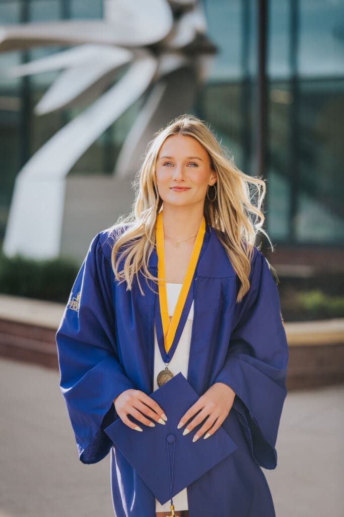 College graduate in purple cap and gown at Minnesota State University Mankato during sunset